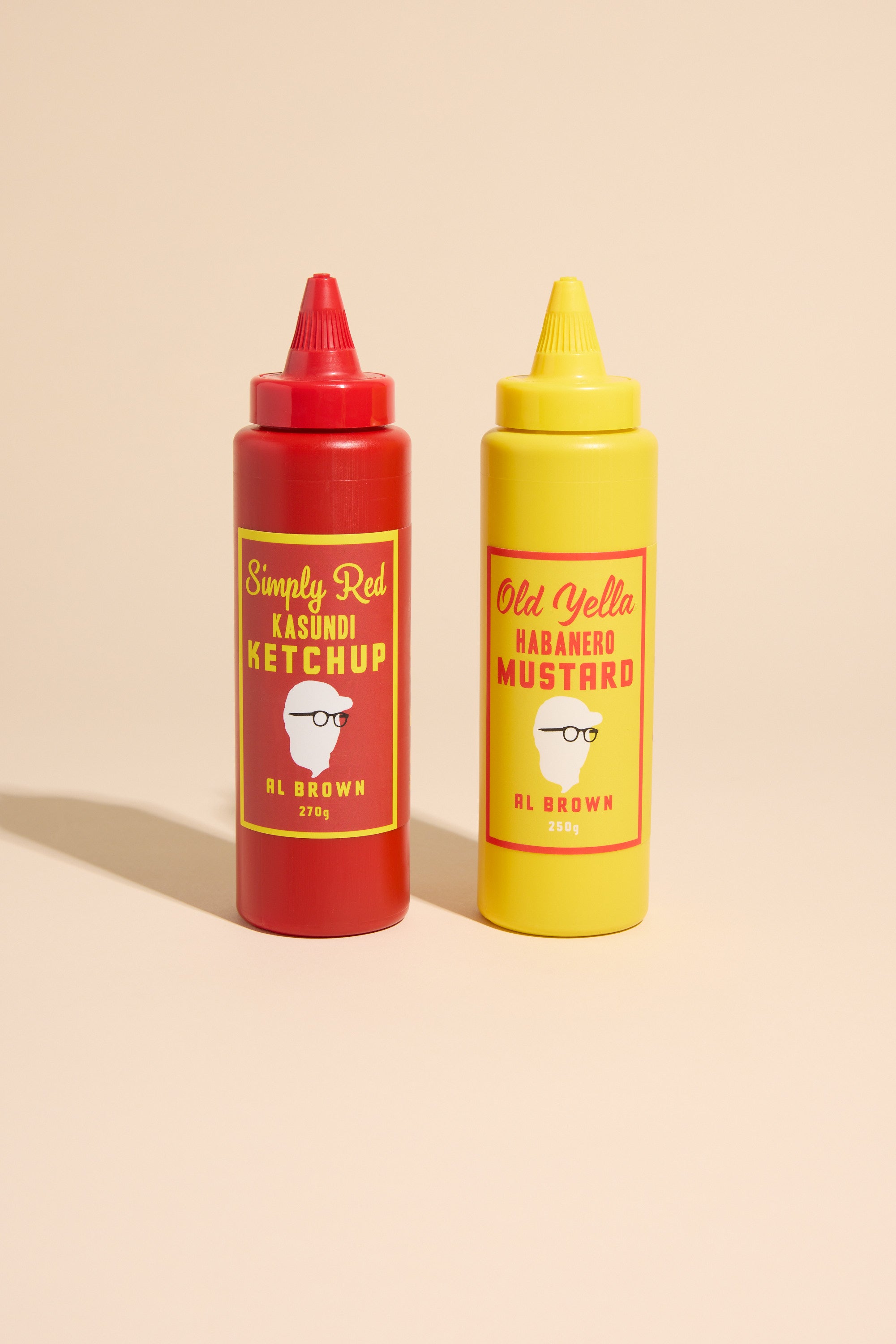 Al's Old Yella & Simply Red Sauce Caddy features two bottles, standing side by side with pointed caps, set against a beige background.