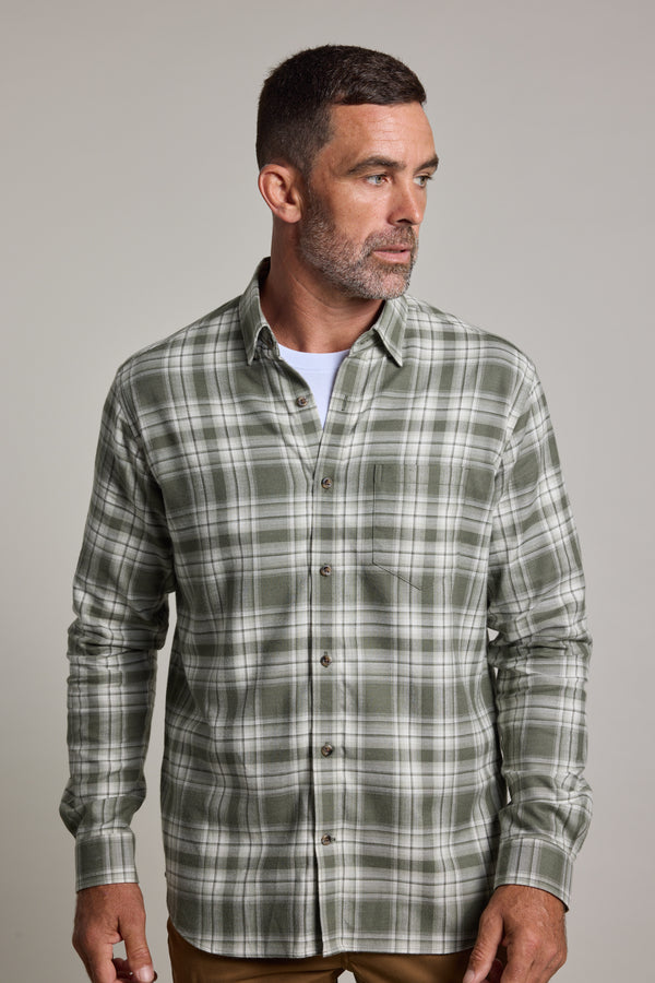A man with short dark hair and a beard wears a Barkers Paxtonheck Shirt, a green check classic fit shirt over a white undershirt, standing against a plain light gray background and looking slightly to his left.