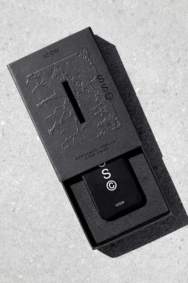 A black rectangular Solid State - Icon perfume bottle with white "ICON" text is partially slid from a matching textured box, set on a light gray surface. The packaging reflects Australian scents: Bergamot • Vanilla • Star Anise.