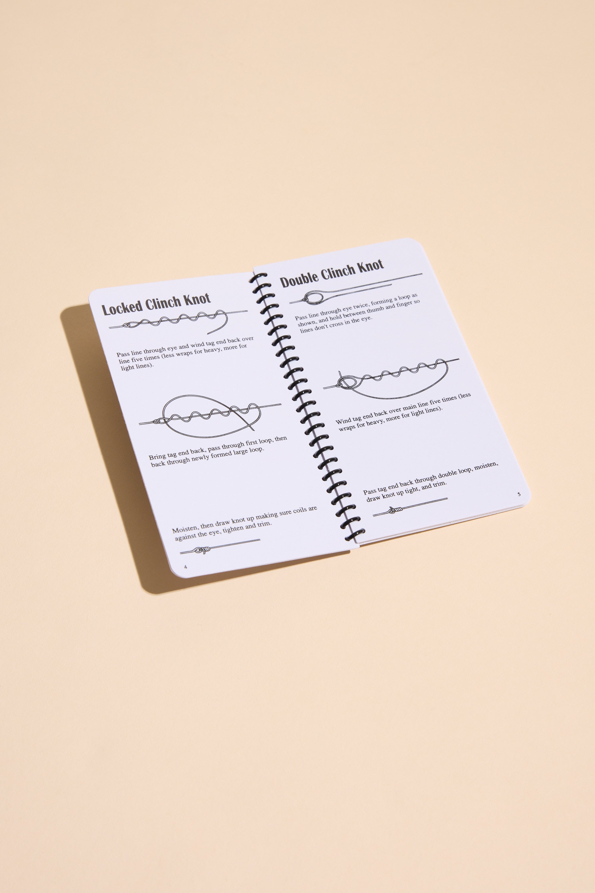 The "Fishing Knots" book by Other lies open on a beige surface, displaying clear illustrated instructions for tying the Locked Clinch Knot and Double Clinch Knot with simple line drawings and descriptive text.