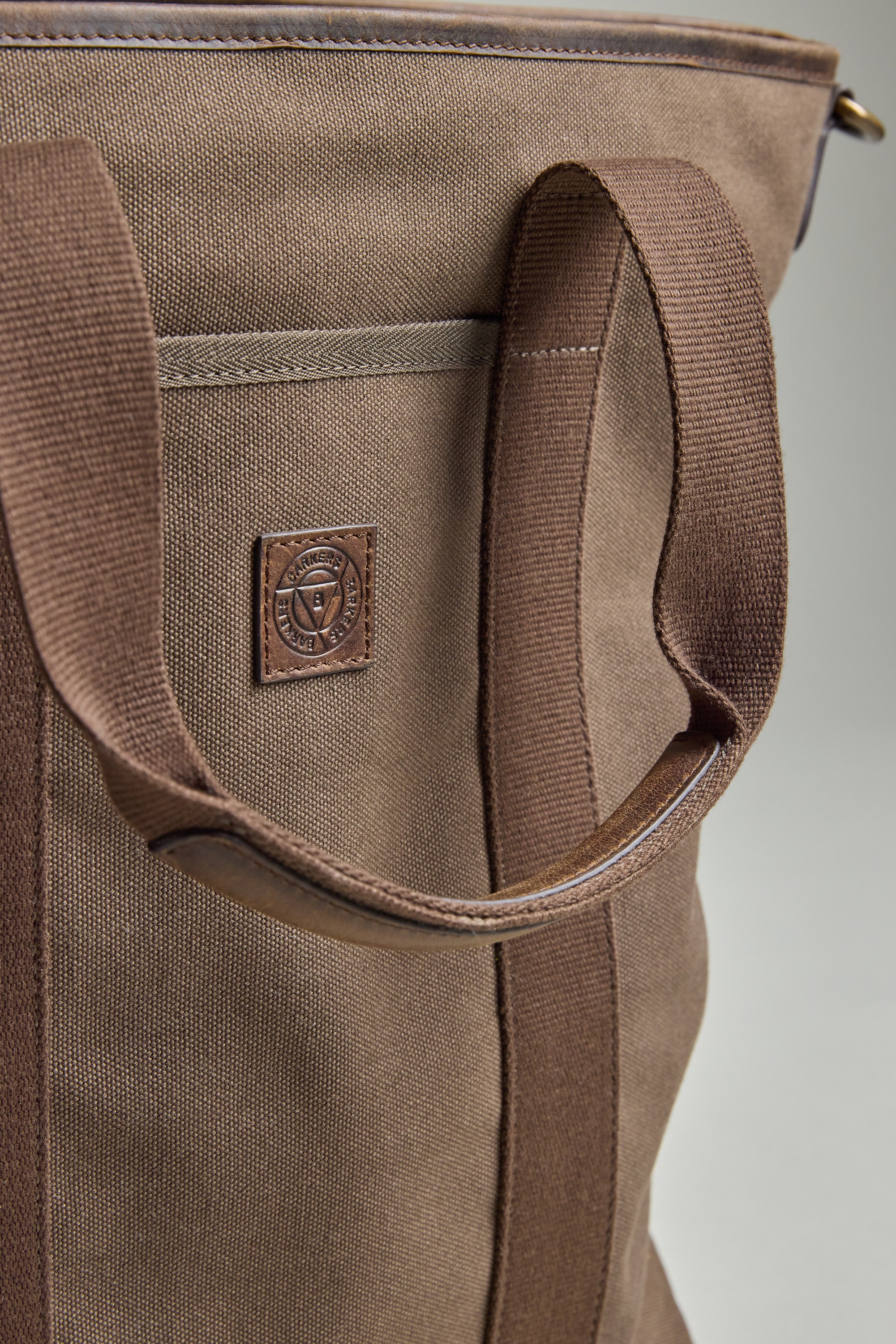 Close-up of the Foxton Canvas Convertible Tote by Barkers, showing its brown cotton canvas, sturdy handles, and leather patch with embossed logo. Detailed stitching and fabric texture highlight the quality craftsmanship.