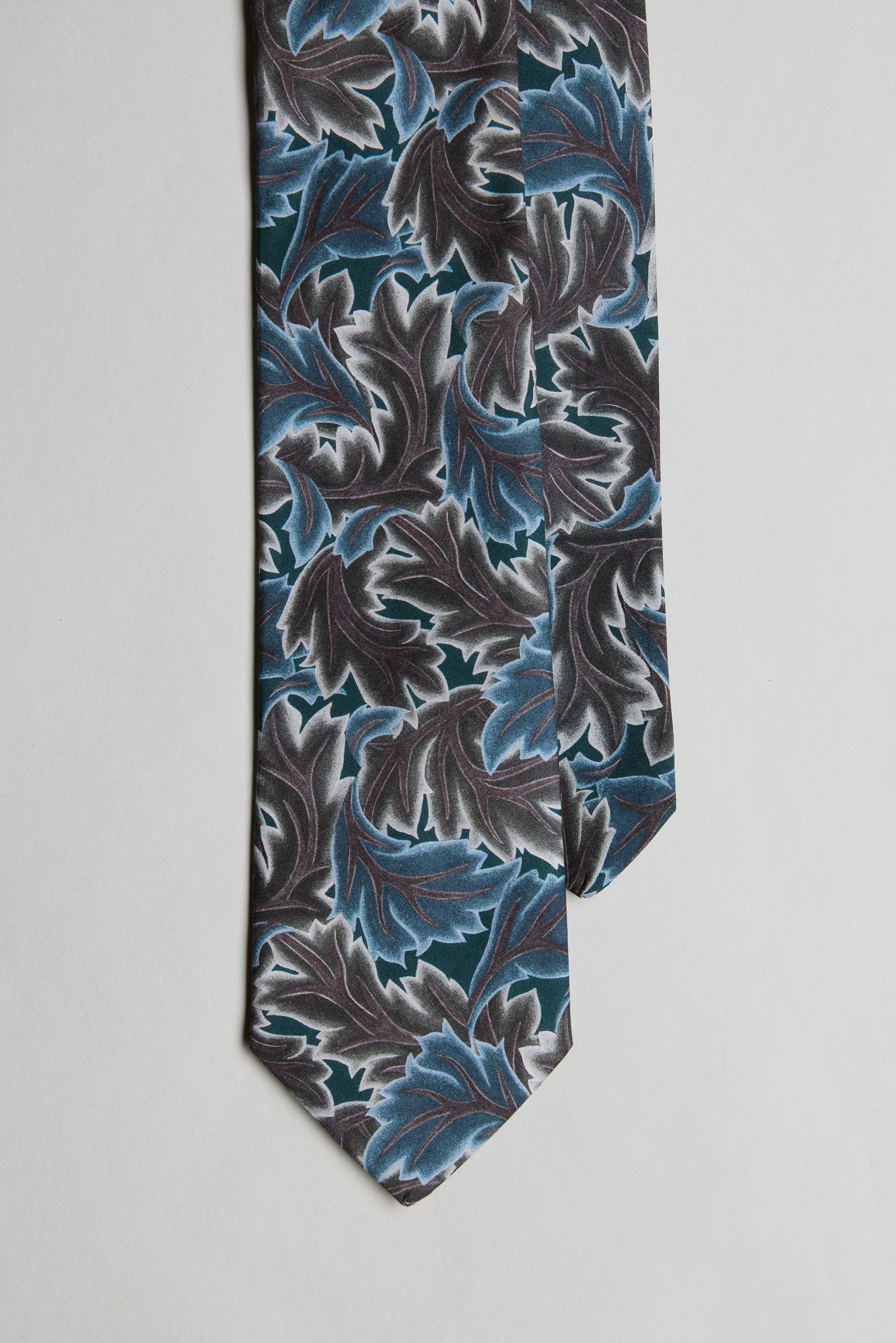 The Liberty Midnight Canopy Tie by Liberty is a men's formal accessory, featuring bold blue, teal, and gray leaf patterns on black Tana Lawn cotton, presented on a light gray background.