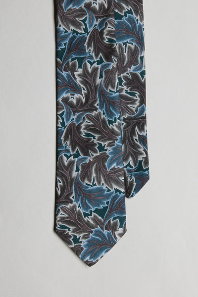 The Liberty Midnight Canopy Tie by Liberty is a men's formal accessory, featuring bold blue, teal, and gray leaf patterns on black Tana Lawn cotton, presented on a light gray background.