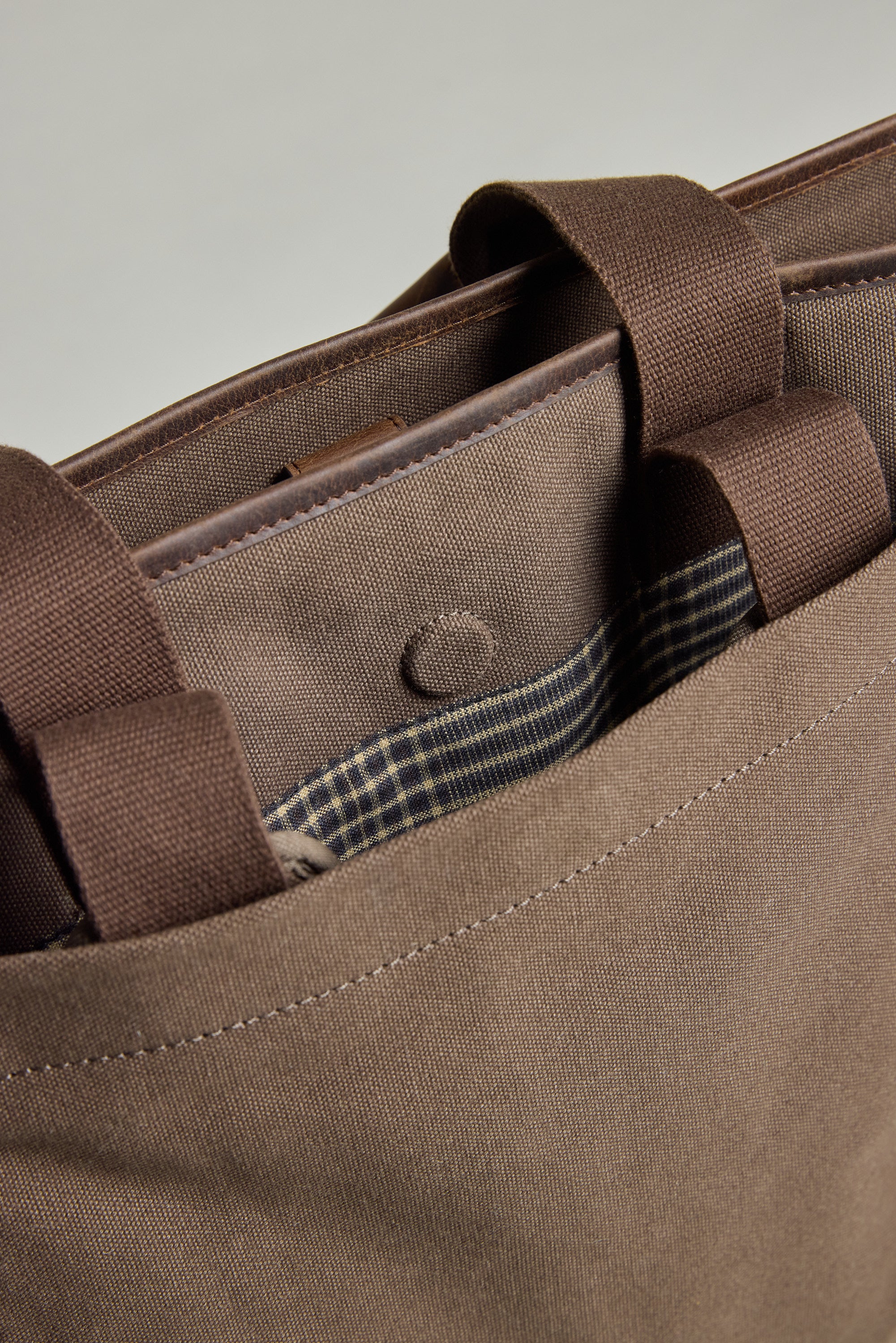 Close-up of the Barkers Foxton Canvas Convertible Tote, a brown cotton bag with handles, snap button closure, and a partially visible pocket lined with checkered fabric.