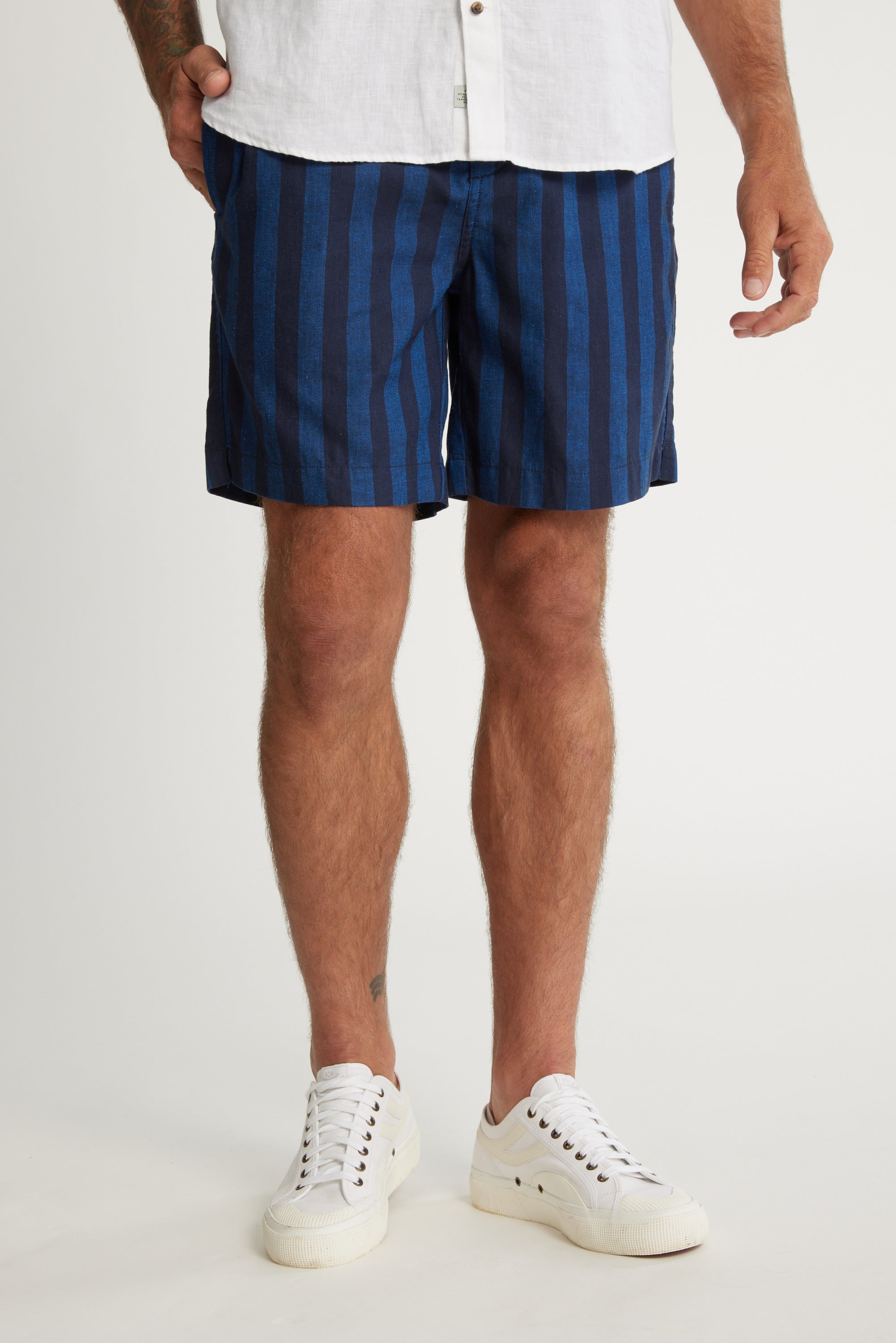 Wearing white sneakers, a white shirt, and Barkers Ashbury Stripe Short in a relaxed fit, a person stands against a light background. The photo captures them from mid-torso to feet.