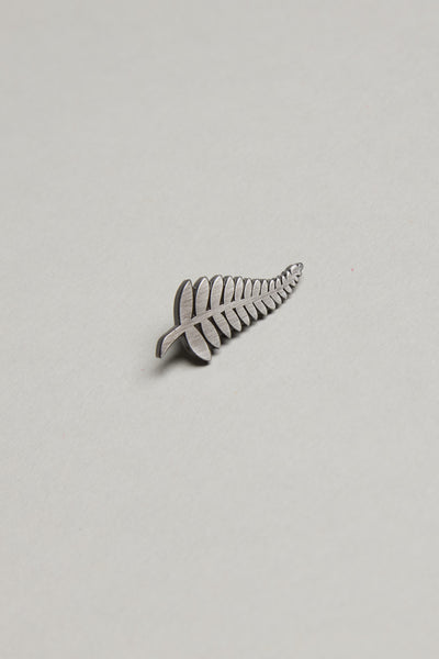 The Barkers Classic Fern Lapel Pin, featuring a brushed silver finish, rests on a plain light gray background—an ideal accessory to elevate any formal outfit.