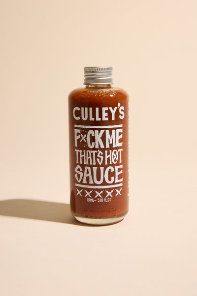 A bottle of Culley's F@#k Me That's Hot Sauce features bold white text on a light beige label. This New Zealand hot sauce packs Carolina Reaper heat in fiery red sauce, sealed with a metal cap.