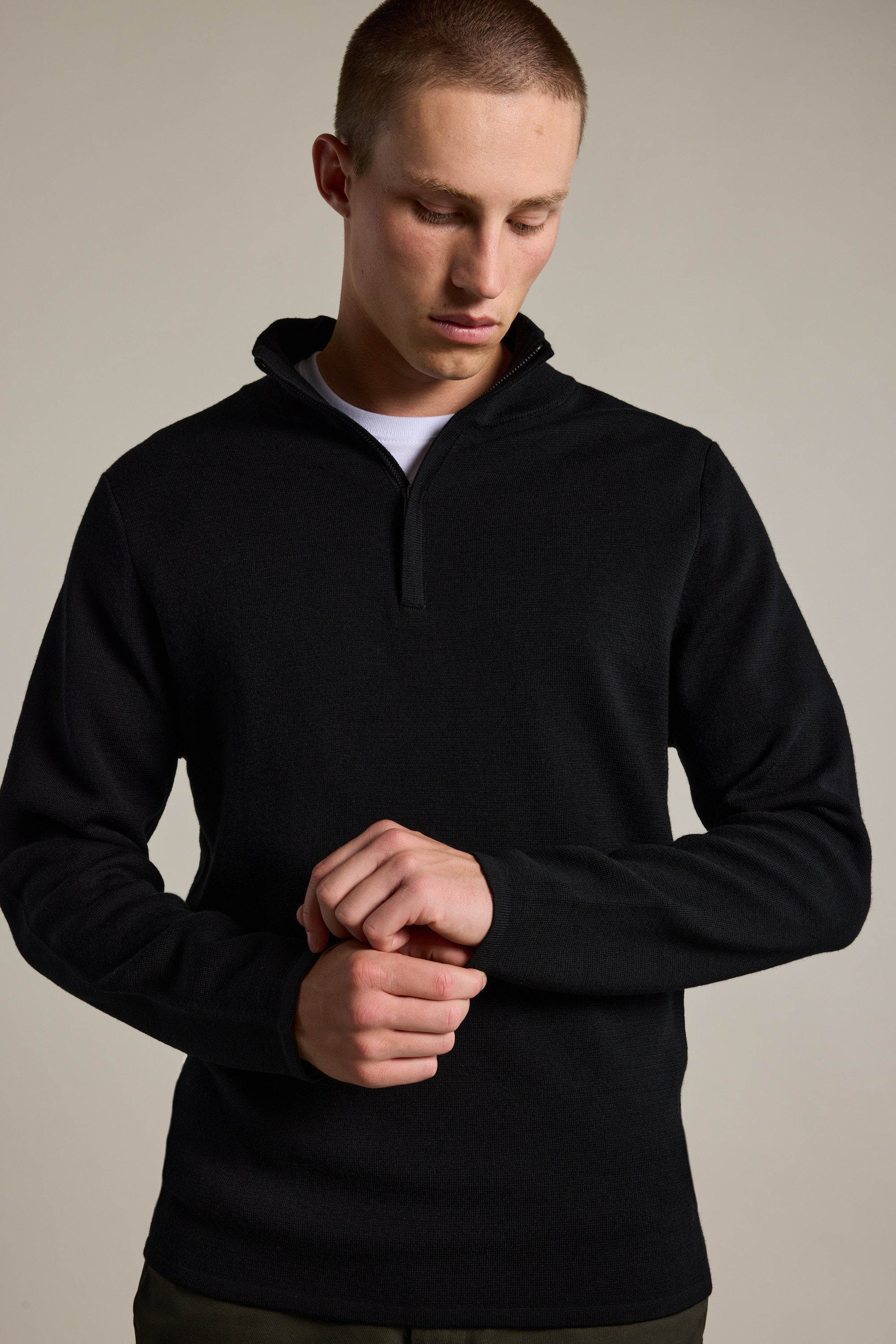 A person wears the Barkers Brandon ZQRX Merino 1/4 Zip pullover in black over a white shirt, standing against a plain background and adjusting their sleeve—ideal for cold-weather layering.