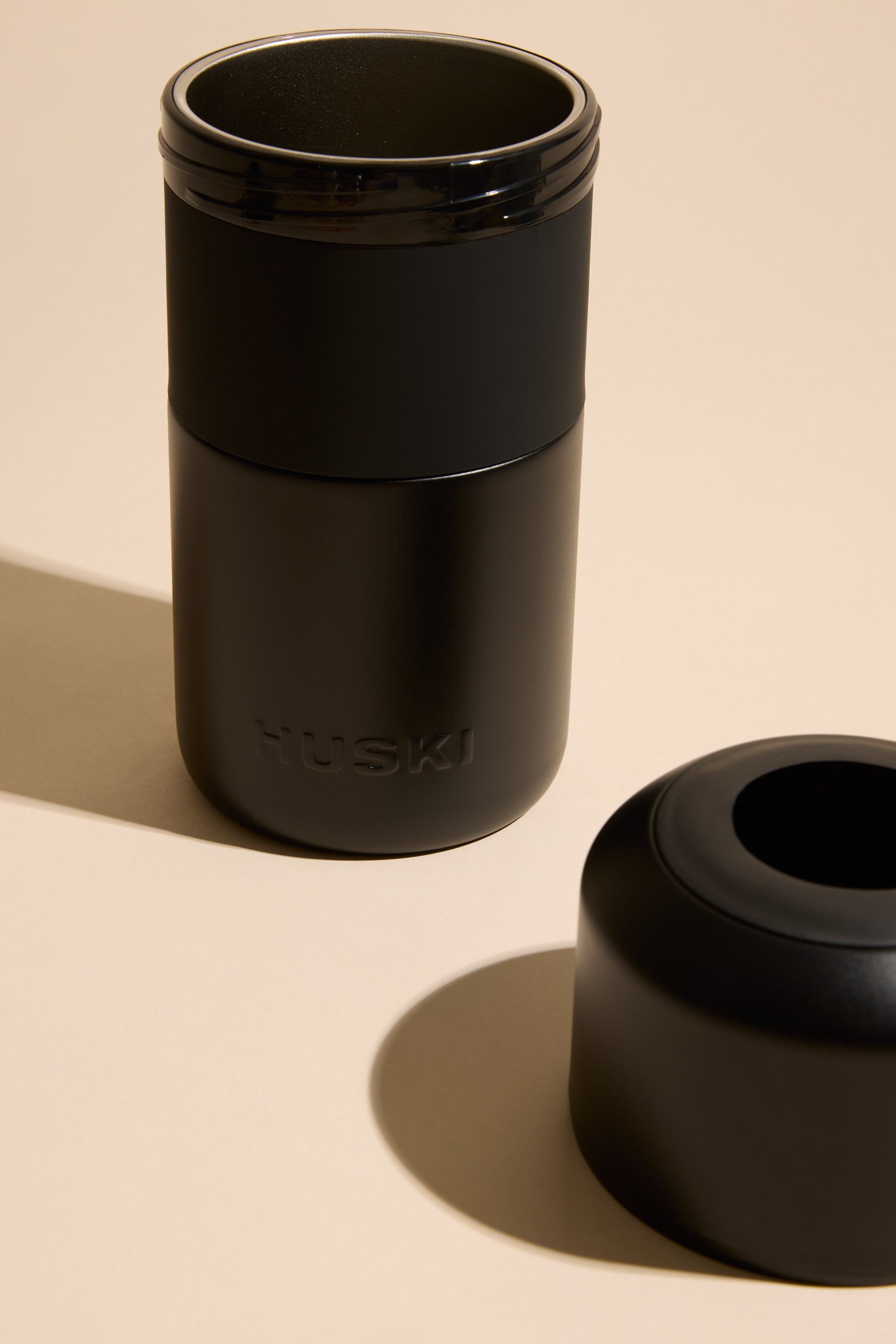 The Huski Wine Cooler by Huski, made from black stainless steel, stands upright on a beige surface next to its lid. This stylish cooler keeps your wine cold for hours.