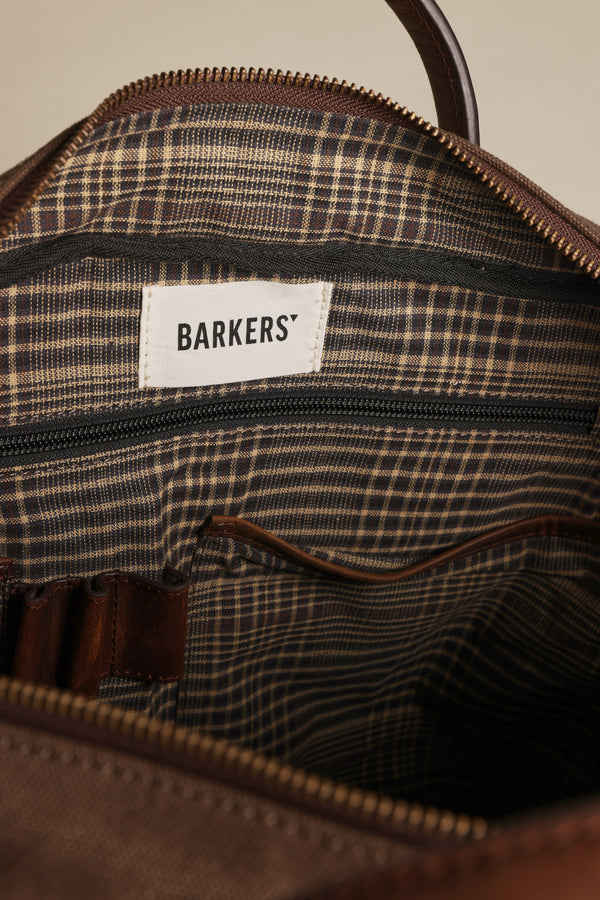Close-up of the Redford Canvas Laptop Bag by Barkers, featuring a plaid fabric lining, zippered pocket, and white "BARKERS" label. Its open interior reveals organized compartments—ideal for carrying your laptop in style.