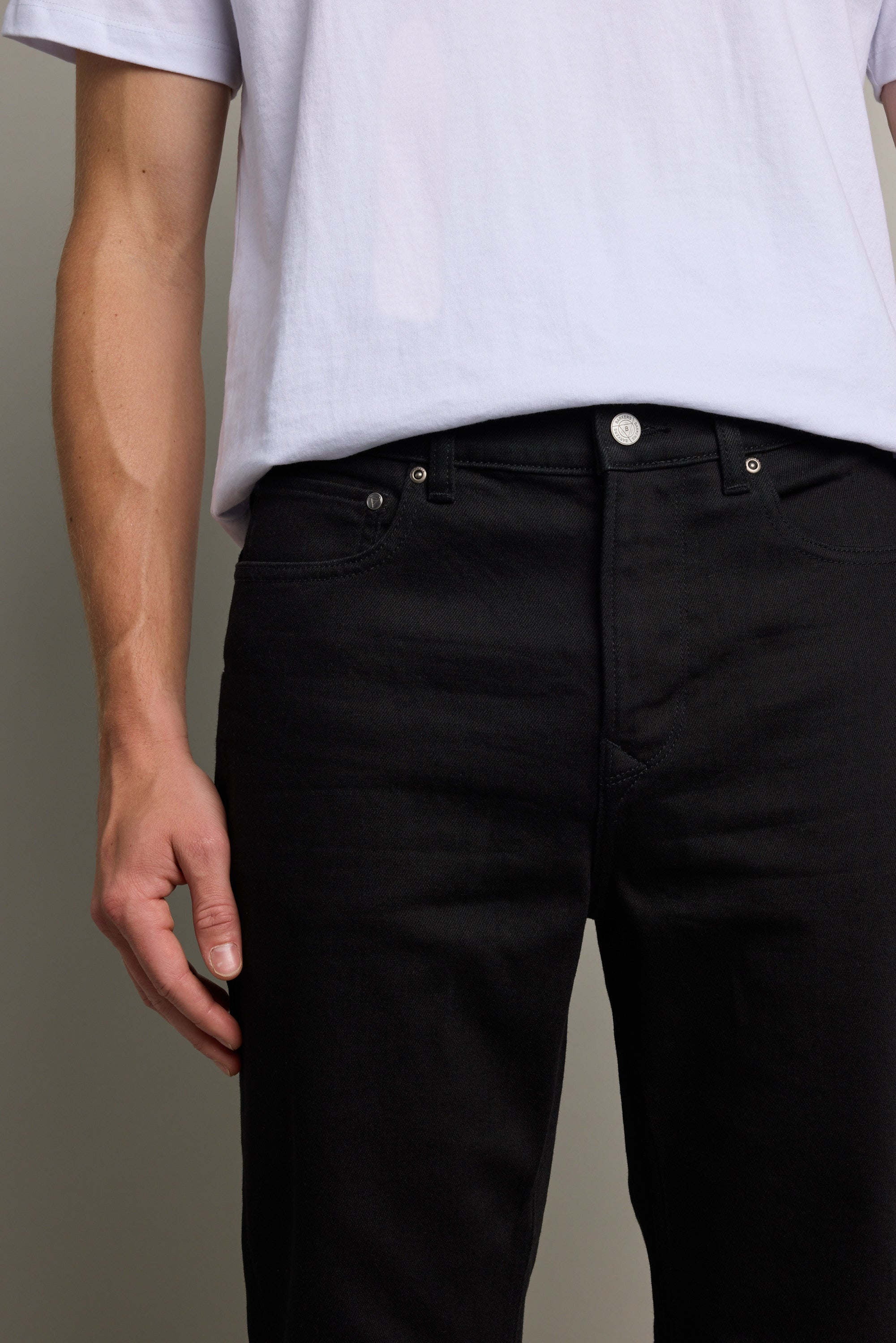 A person wearing a white t-shirt tucked into Barkers Rambler Denim Slim Jeans, shown from shoulders to mid-thigh, with their left arm relaxed by their side.