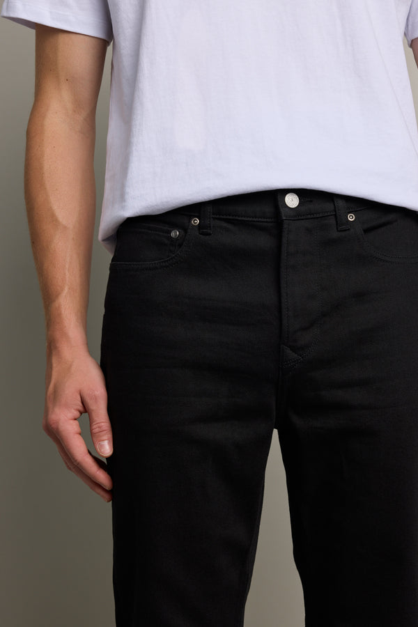 A person wearing a white t-shirt tucked into Barkers Rambler Denim Slim Jeans, shown from shoulders to mid-thigh, with their left arm relaxed by their side.