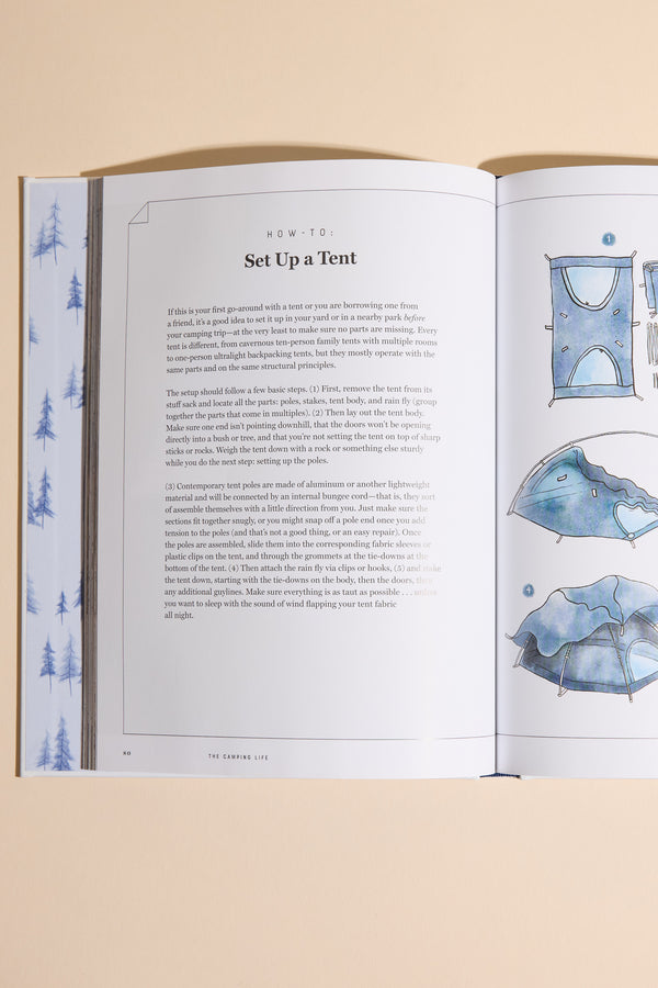 The "Camping Life" book by Other is open on a beige surface, displaying tent setup instructions with blue assembly illustrations and watercolor-style tree patterns that capture the spirit of outdoor adventure.