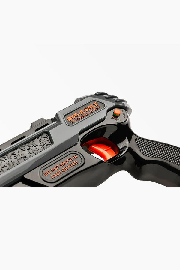 Close-up of a Bug-A-Salt 3.0 Black Fly by Other, showing its black finish, trigger, safety switch, and warning label: “DO NOT SHOOT IN FACE OR EYES.”.