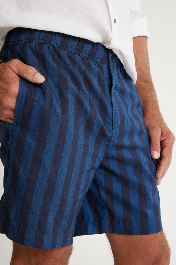 A person in a white shirt and Barkers Ashbury Stripe Short stands with one hand in their pocket, showcasing the comfort and style of these cotton linen shorts. The image highlights the shorts and lower torso.
