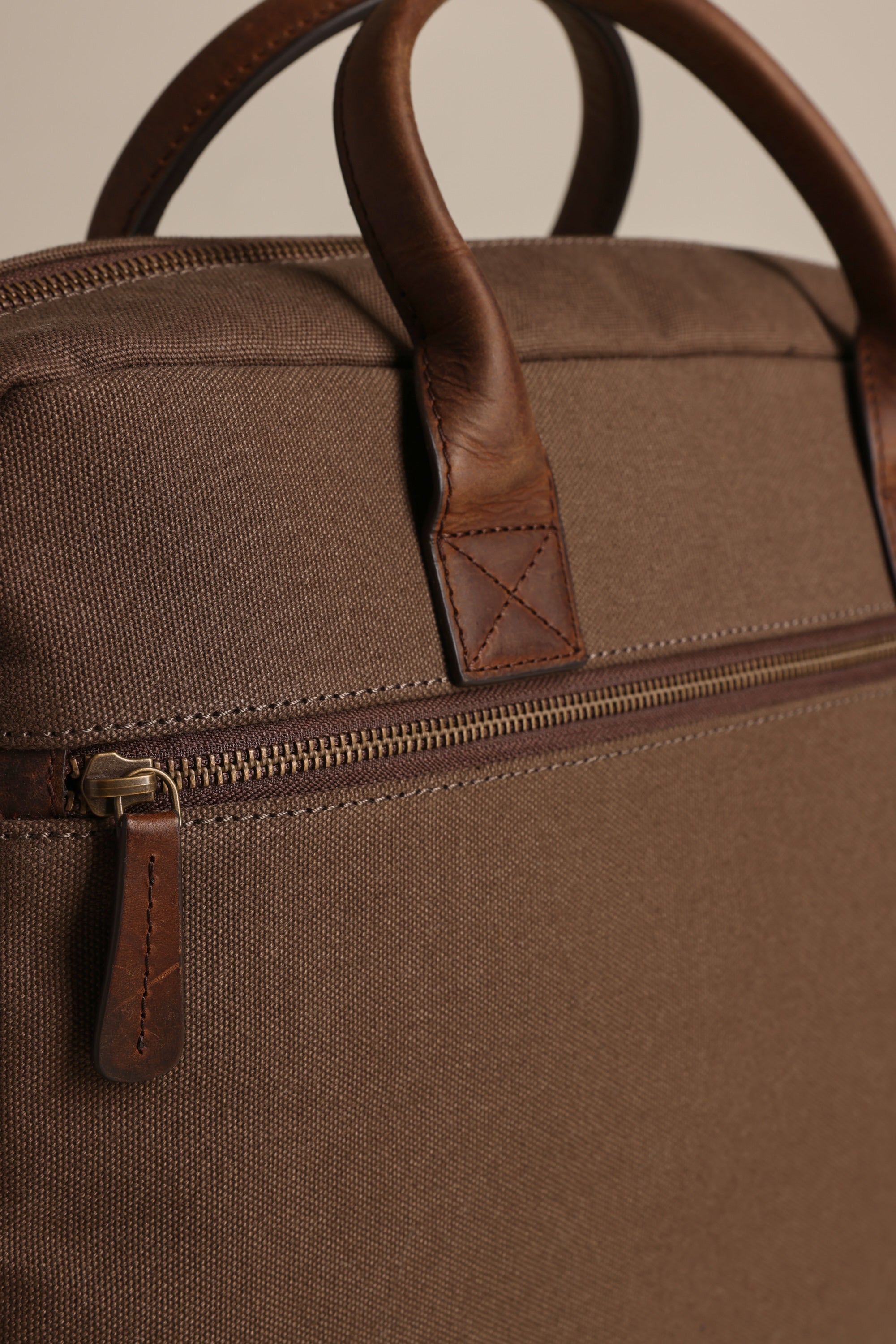 Close-up of the Barkers Redford Canvas Laptop Bag, featuring premium leather handles, a zippered pocket with a leather pull tab, and visible stitching on both the bag and handles.