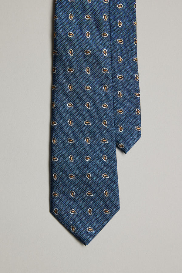 The Kamler Paisley Tie by Barkers is a blue silk tie with a small repeating paisley print in brown, white, and black, shown on a plain light gray background.