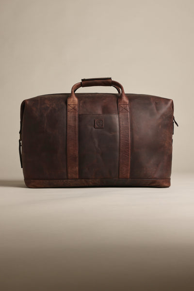 The Barkers Costello Leather Weekender is a large, dark brown men’s bag with sturdy straps and a top handle, crafted from premium leather luggage, shown against a neutral beige background.