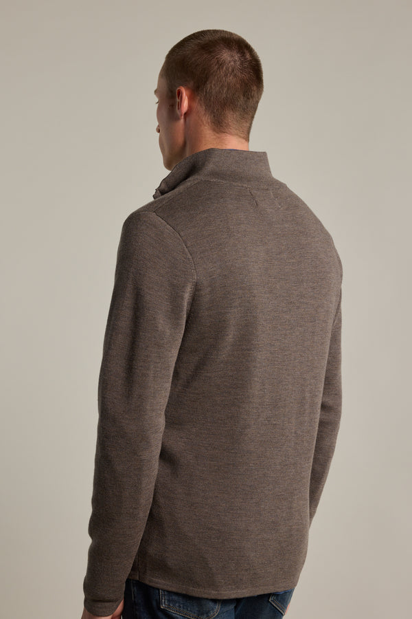A person wearing the Barkers Brandon ZQRX Merino 1/4 Zip sweater in brown, styled as a layering piece with blue jeans, stands with their back to the camera against a plain light background.