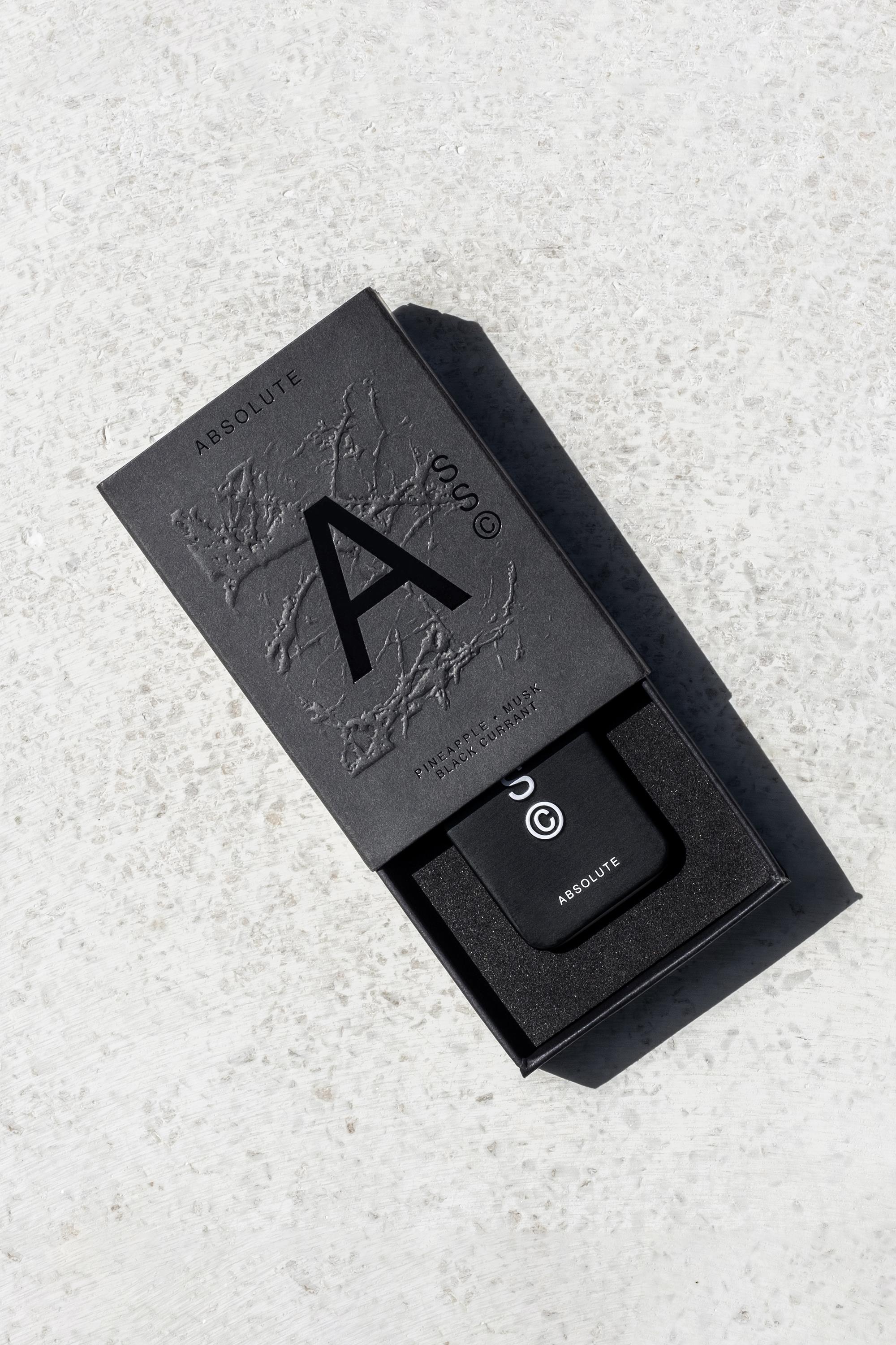 A sleek black box labeled Solid State - Absolute with a bold "A" and textured design sits partially open on a light gray surface, revealing a pocket-sized black cologne container inspired by Creed Aventus from Solid State inside.