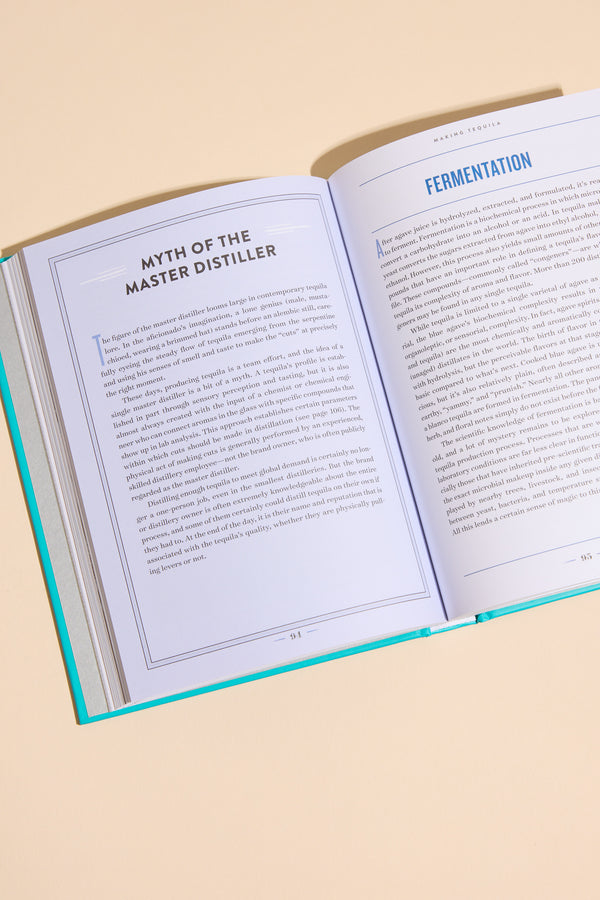 An open book, A Field Guide To Tequila by Other, rests on a beige surface. Its blue-bordered pages titled "Myth of the Master Distiller" and "Fermentation" are visible, suggesting an in-depth guide to tequila.
