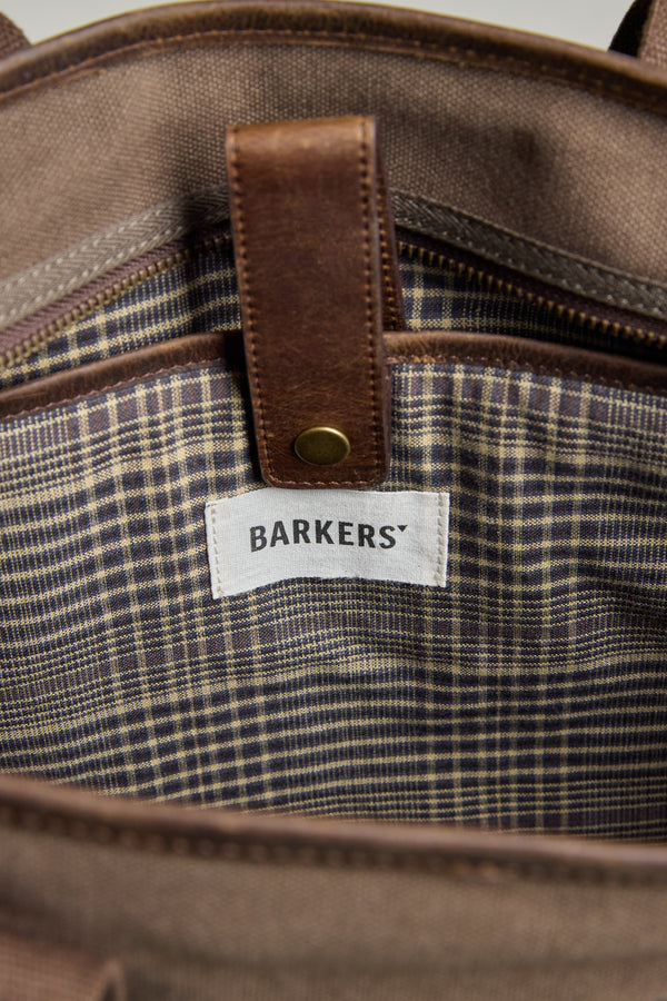 Close-up of the Foxton Canvas Convertible Tote by Barkers, showing its plaid fabric lining and a white Barkers label under a brown leather strap with a brass snap button.