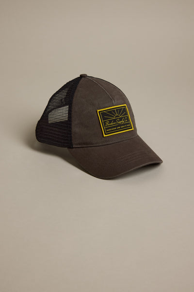 The Barkers Supply Co. Trucker cap by Barkers features a brown front, black mesh back, yellow rectangular patch, and an adjustable fit, shown on a neutral background.