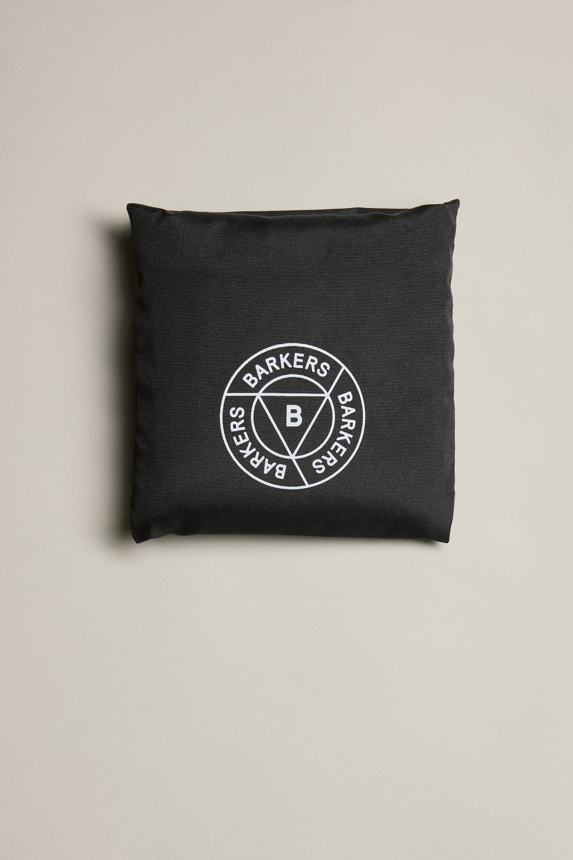 The Barkers Shopping Bag is a black square pouch crafted from recycled polyester bag material, featuring a white circular Barkers logo at the center—perfect for everyday carry. Shown on a plain, light beige surface.