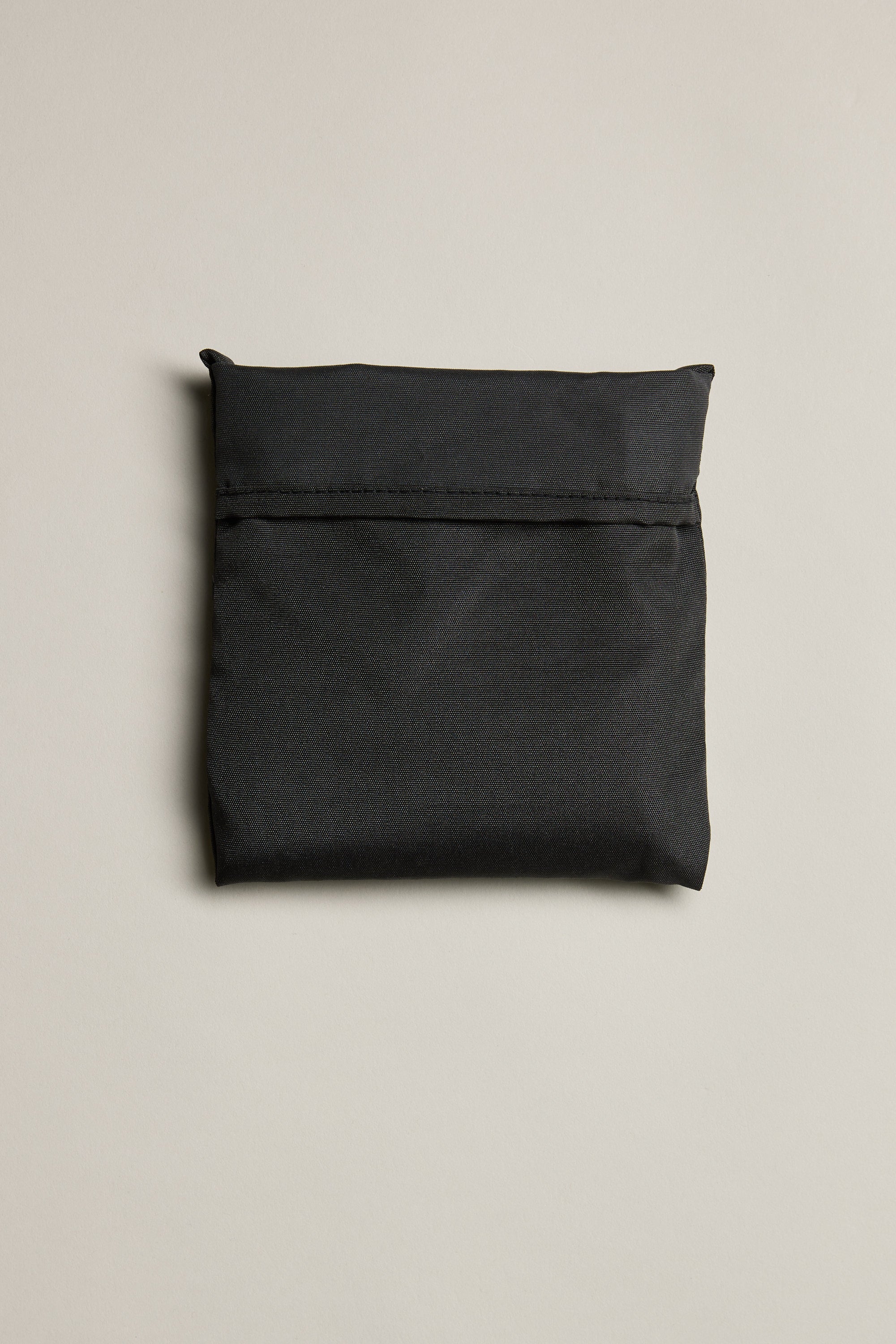 The Barkers Shopping Bag, a closed flat black bag made from recycled polyester, is shown with a horizontal flap on a plain light beige background.