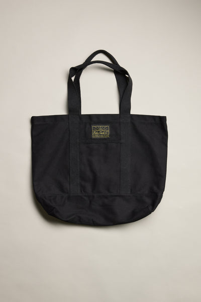 The Barkers Supply Co. Canvas Tote Bag by Barkers features two handles and a small rectangular patch label at the top center. Made from durable black canvas, it's displayed against a plain light background.
