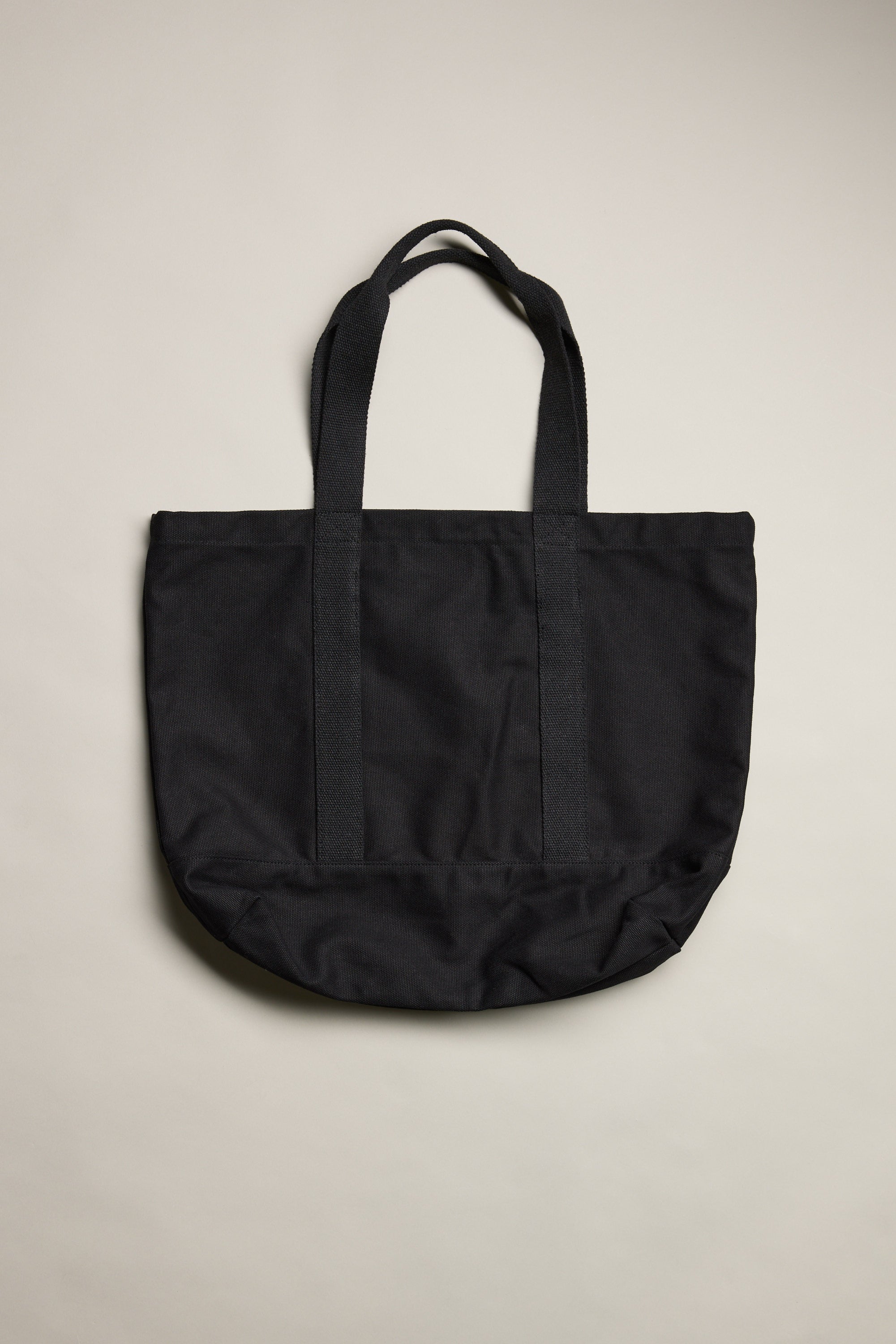 The Barkers Supply Co. Canvas Tote Bag by Barkers, made from durable black canvas with two handles, lies flat on a neutral light background.