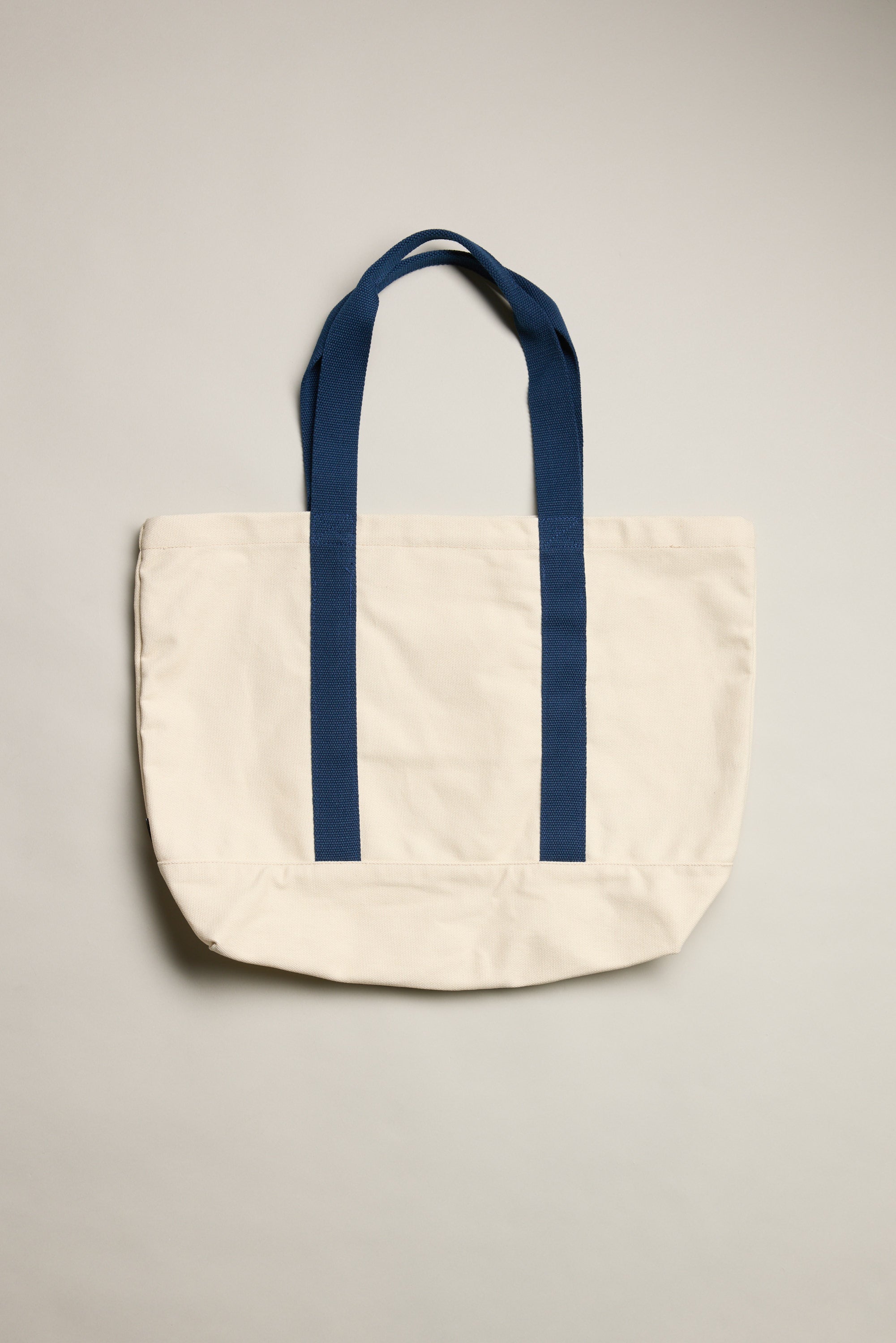 The Barkers Supply Co. Canvas Tote Bag by Barkers features dark blue handles and trim on durable canvas, photographed against a light background. This versatile travel tote's simple, unadorned design is complemented by its neatly arranged handles.