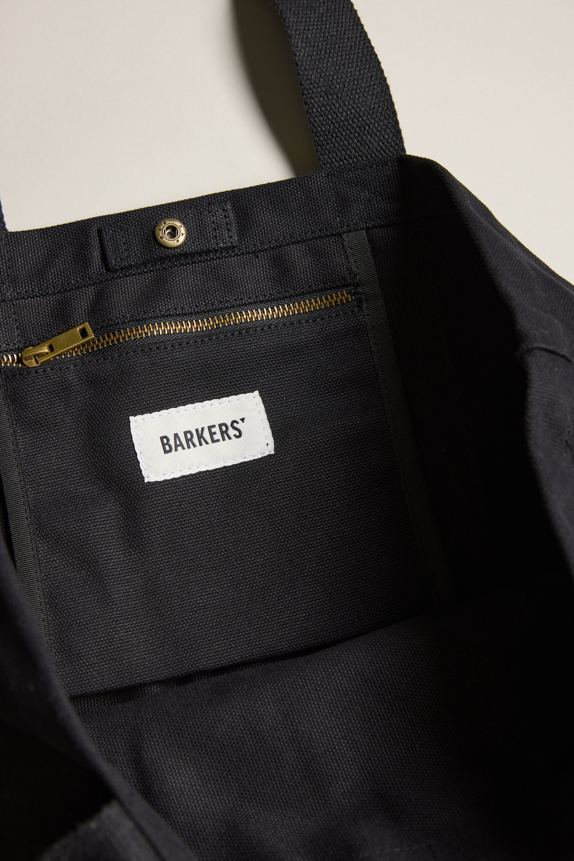 Close-up of the Barkers Supply Co. Canvas Tote Bag interior, showing a gold zipper pocket, snap button, and a white Barkers label sewn onto the durable black canvas lining.