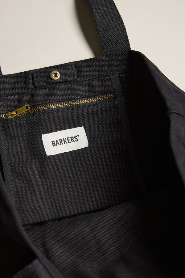 Close-up of the Barkers Supply Co. Canvas Tote Bag interior, showing a gold zipper pocket, snap button, and a white Barkers label sewn onto the durable black canvas lining.