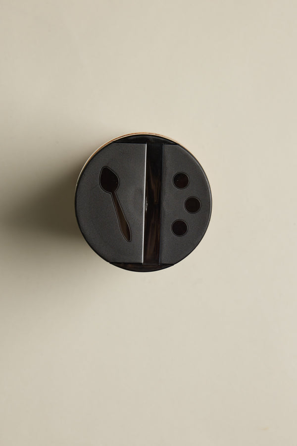 A black plastic lid on The Pork Rub 295g by Other, viewed from above, with a spoon-shaped slot and three small holes—ideal for sprinkling BBQ seasoning or smoked paprika—set against a plain light background.