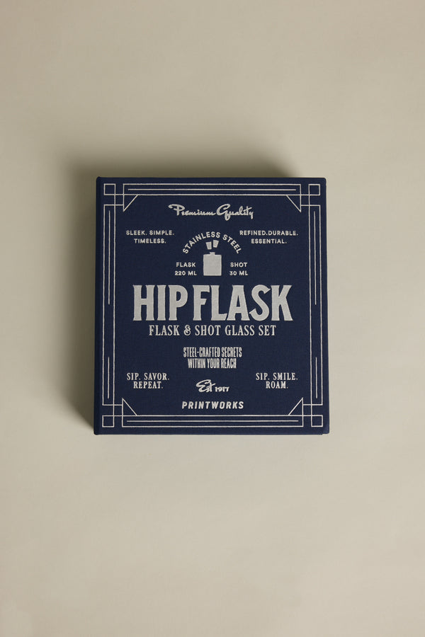 A navy blue box with "The Essentials Hip Flask" in white vintage-style text by Barkers highlights a stainless steel flask and shot glass set, showcasing quality, craftsmanship, and timeless appeal.