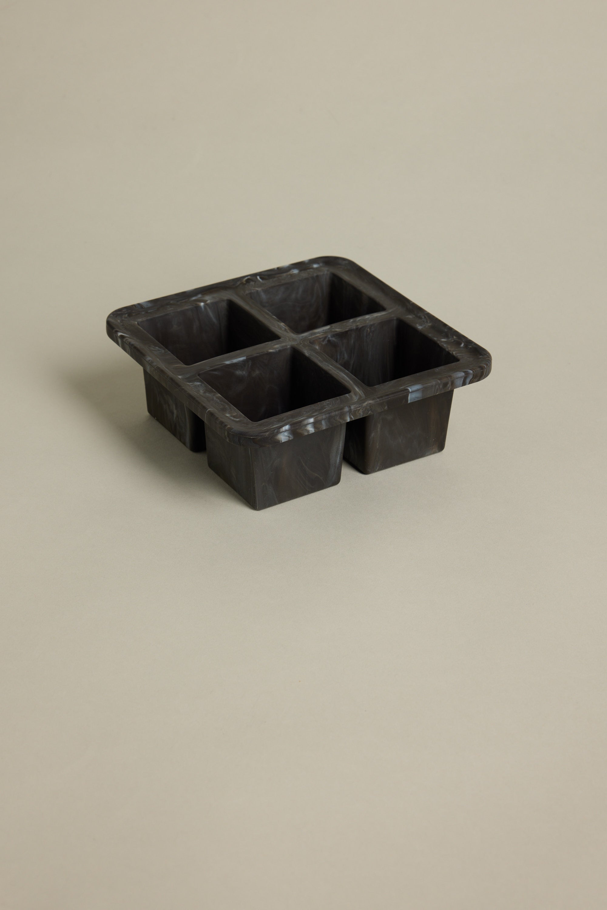 The Other Ice Tray Sphere Marble Black, a black silicone tray with four large compartments for slow-melting ice in your home bar, is set on a plain beige background.