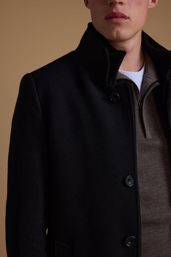 A person wearing a black Barkers Raymond Coat over a brown zip-up sweater and white shirt, shown from the chest up against a plain beige background, with their face partially visible.