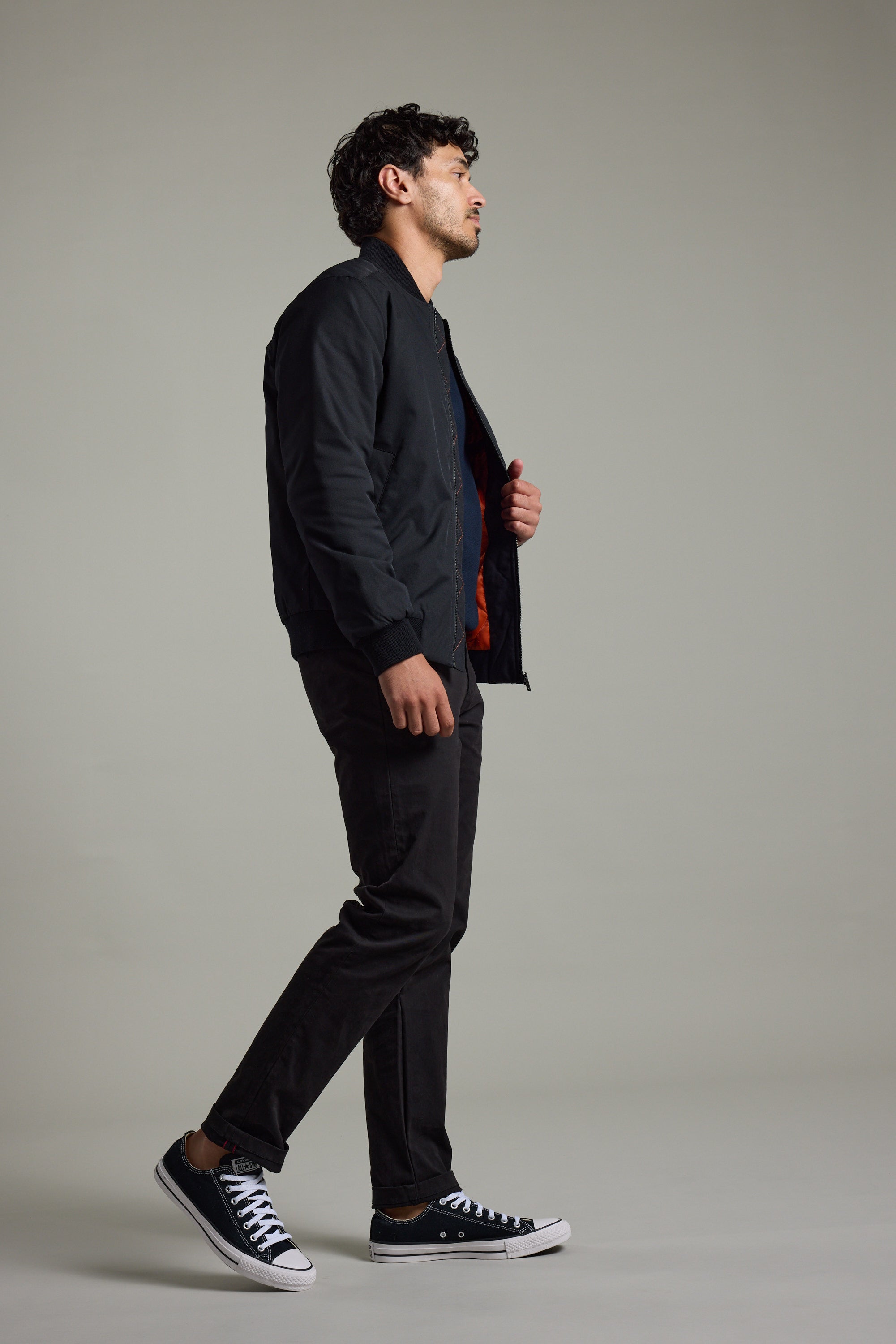 Man in a Barkers Dunhill Bomber Jacket, black pants, and sneakers stands sideways, plain background.