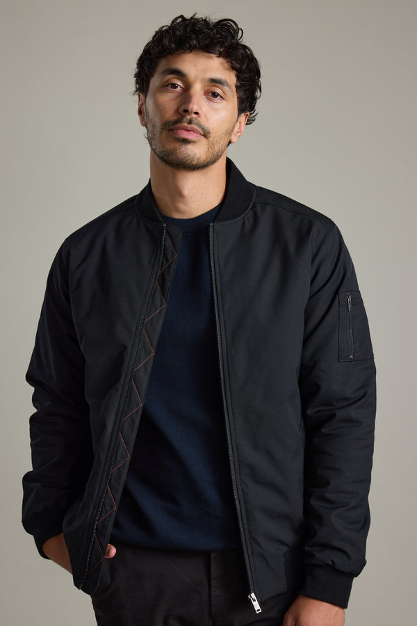Man with short curly hair wears a Barkers Dunhill Bomber Jacket and navy shirt against a plain background.