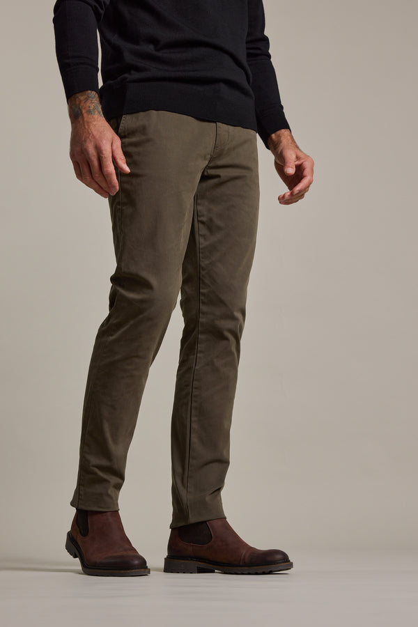 A person stands against a neutral background, wearing Barkers Carnaby Chino in olive green, a black long-sleeve sweater, and brown Chelsea boots. The photo is cropped from mid-torso down.