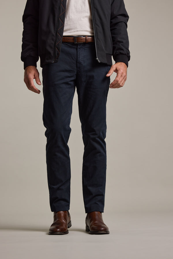 A man stands facing forward, wearing a dark jacket, white shirt, Barkers Carnaby Chino, brown leather belt, and brown leather shoes. The image is cropped at the shoulders.