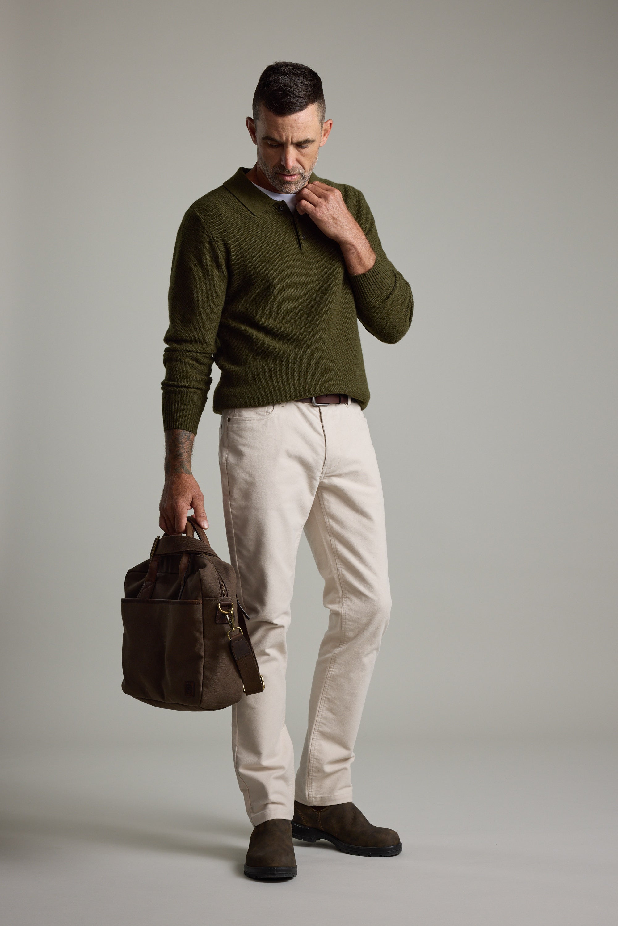 Man in Barkers Ainsley Woollen Long Sleeve Polo and light pants, holding a brown bag.