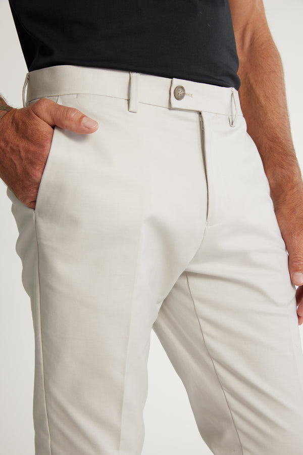 A person models Barkers Lyndon Cotton Pants in light beige, one hand in the pocket, paired with a black shirt. The cropped photo highlights the lower torso and upper legs, showcasing a smart casual style.