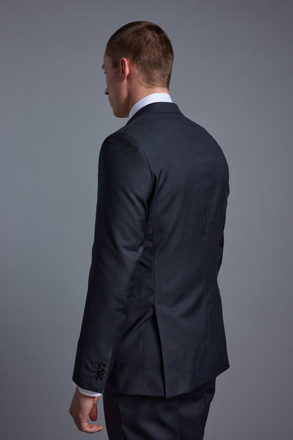 A man wearing a dark Barkers Mayfair ZQ Suit Jacket, crafted from premium New Zealand Merino, stands with his back to the camera and head turned slightly left against a plain gray background.