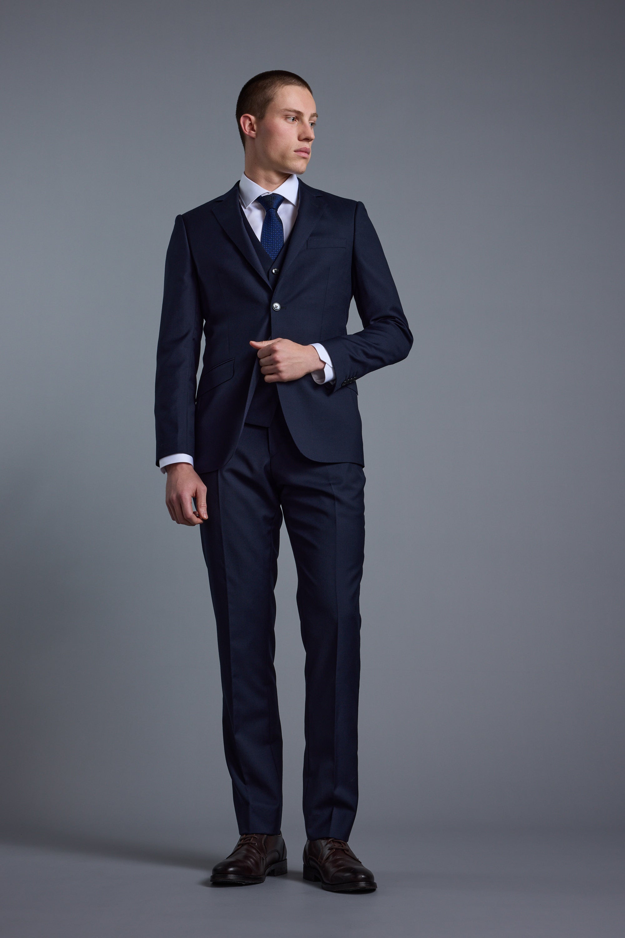 Man in Barkers Mayfair ZQrx Suit Trouser, white shirt, and tie against a gray background.