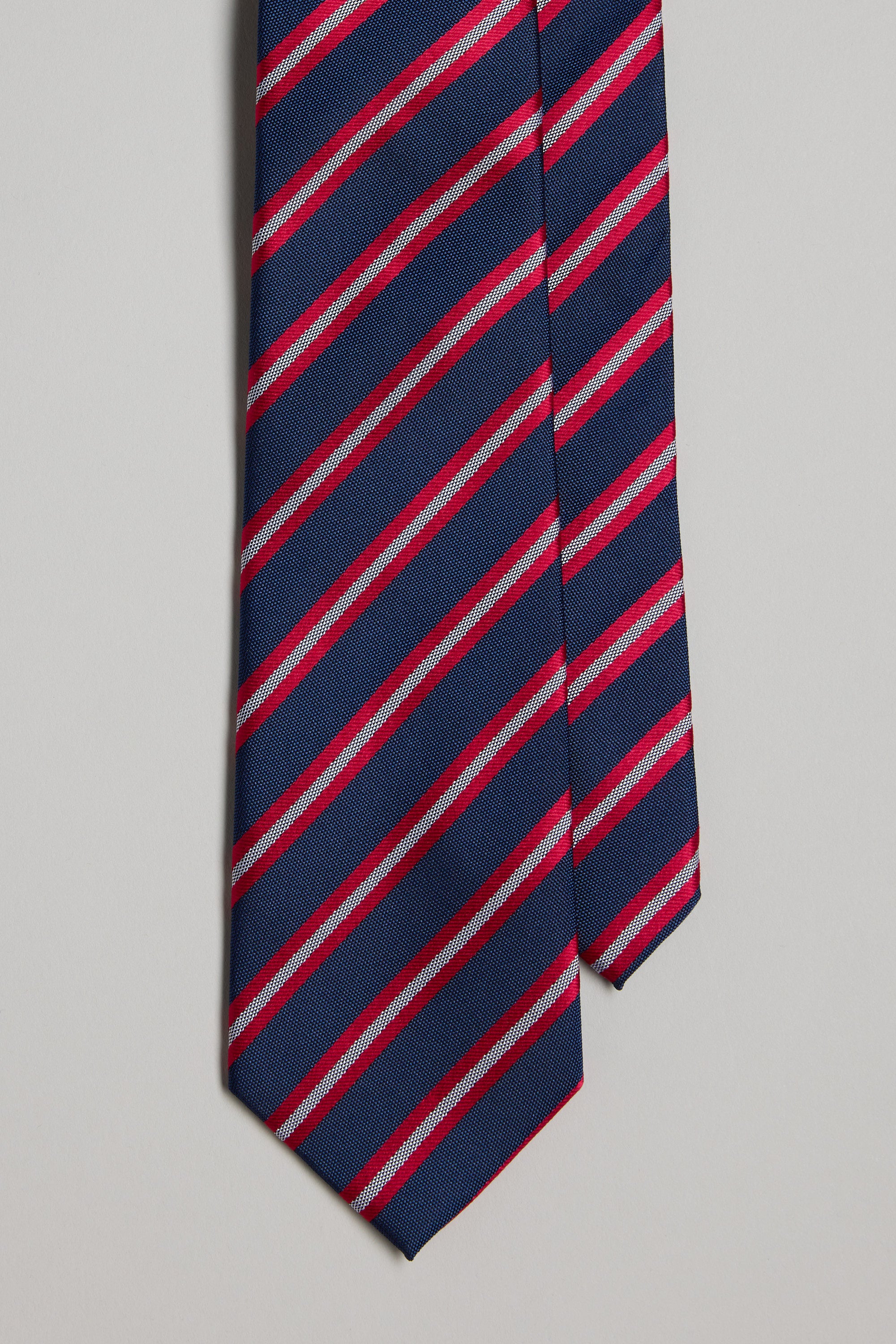 A close-up of the Willem Stripe Tie by Barkers, featuring navy blue silk with red and light gray diagonal stripes against a plain background—a classic accessory perfect for pairing with pocket squares or other silk accents.