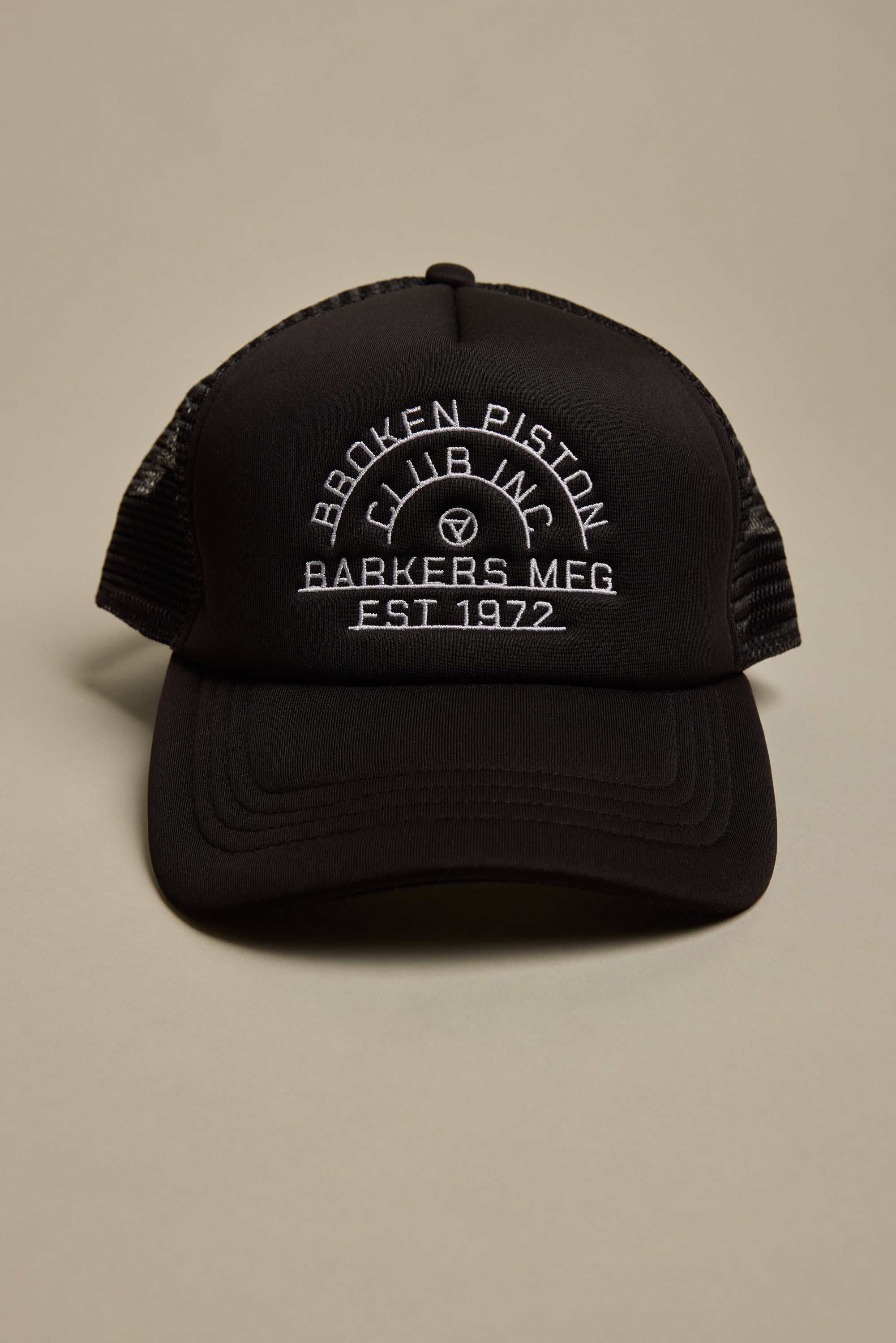 The Barkers Piston Club Trucker Cap is a black cap with mesh sides, an adjustable fit, and a front white embroidered logo that reads: BROKEN PISTON CLUB INC, BARKERS MFG, EST 1972 in curved and straight lines.