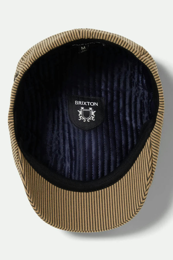 The Brixton Brood Snap Cap, shown from above in tan and black hickory stripe, features a quilted dark lining and an inner label with the Brixton name and crest for vintage flair.
