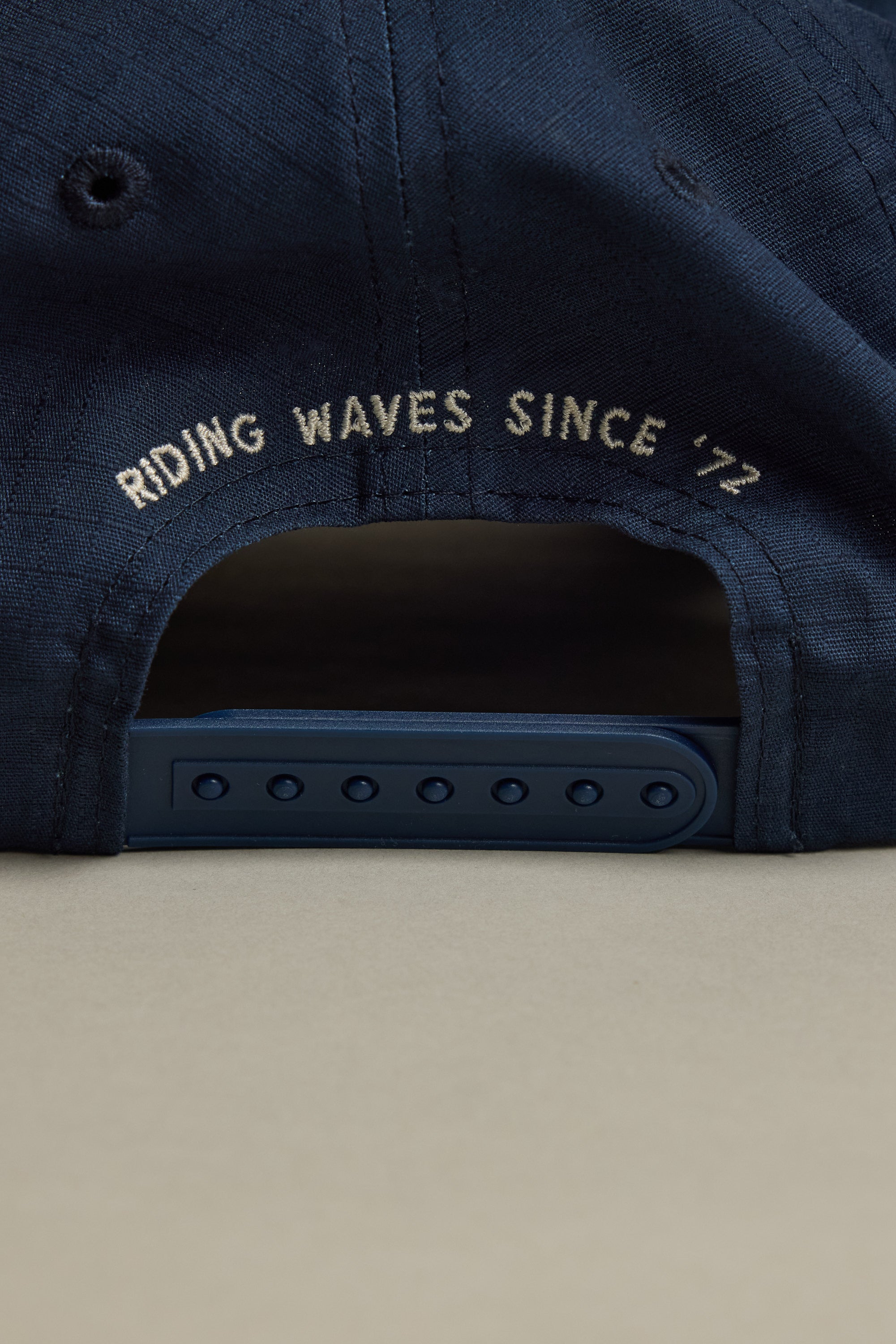 Close-up of the back of the Barkers Wave Master Cap by Barkers, showing an adjustable snapback strap and an embroidered patch with "RIDING WAVES SINCE 72" in white above the opening.